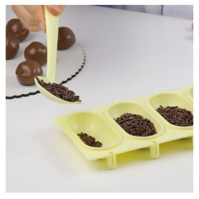 Colher amarela a colocar granulados de chocolate numa forma de silicone amarela para moldar bolas de chocolate