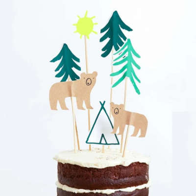 Decoração de bolo com ursinhos, árvores, sol e tenda em cartolina sobre bolo de chocolate com cobertura branca