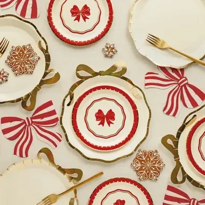Pratos de papel decorativos com laços vermelhos, garfos dourados e biscoitos decorados em forma de flocos de neve
