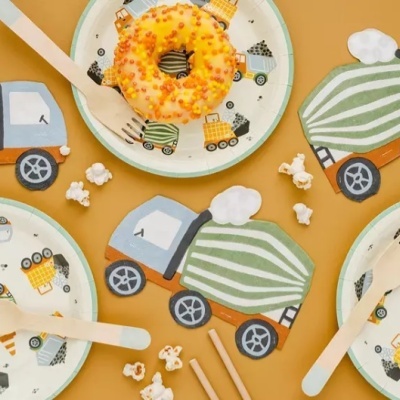 pratos infantis e suportes com padrão de camiões e talheres de madeira numa superfície amarela com bolo e pipocas