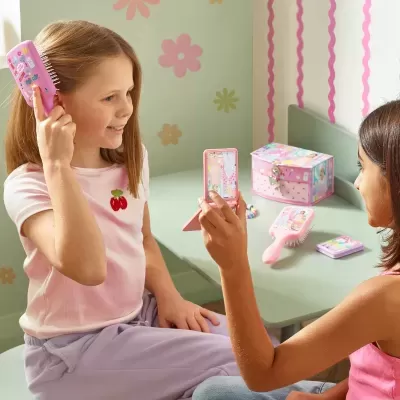 duas crianças brincando com acessórios de pente e espelho rosados decorados com ilustrações coloridas numa divisão com decoração floral