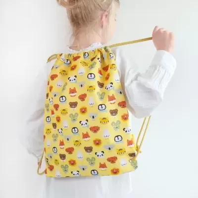 Mochila saco amarelo com estampado de rostos de animais usada por criança