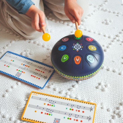 Instrumento musical de língua de aço azul escuro com padrões coloridos e números, baquetas amarelas e partituras coloridas