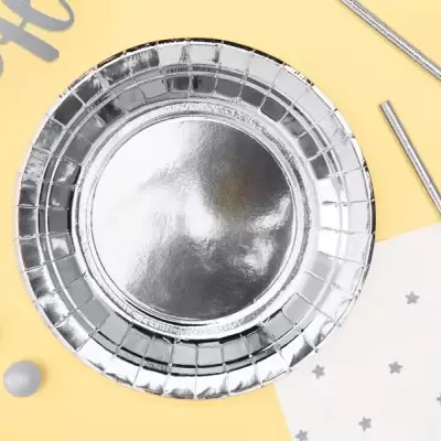 Prato descartável prateado brilhante sobre fundo amarelo e branco com estrelas cinzentas