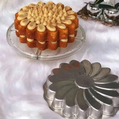 Bolo decorado em forma de flor sobre suporte transparente e forma metálica com padrão de pétalas ao lado