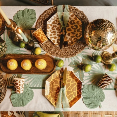 Mesa posta com pratos, copos e guardanapos com padrões de pele de animais, frutas e sobremesas, castiçais dourados