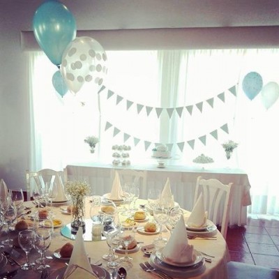 Mesa decorada para festa com toalha bege e balões azuis e brancos ao fundo