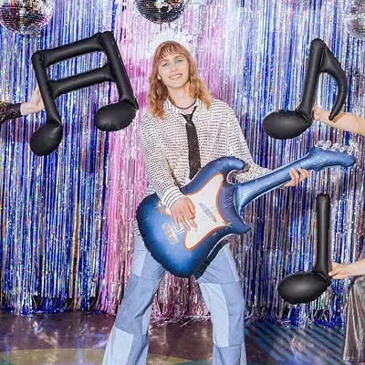 Mulher com guitarra insuflável azul num cenário festivo com notas musicais insufláveis e bolas de espelhos