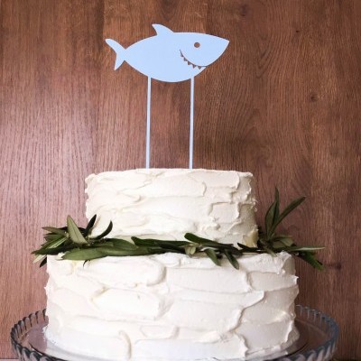 Bolo branco decorado com galhos verdes e topper de tubarão azul