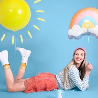 Mulher deitada no chão azul com balões coloridos de hélio