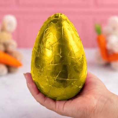 Ovo de chocolate envolto em papel dourado metálico na mão