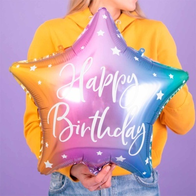 Balão estrela colorido com texto Happy Birthday segurado por pessoa com casaco amarelo.