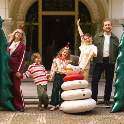Árvores de Natal verdes insufláveis, boneco de neve insuflável branco, família alegre em frente a edifício com arco