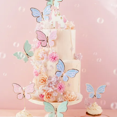 Bolo decorado com flores e borboletas coloridas acompanhado de cupcakes com cobertura creme