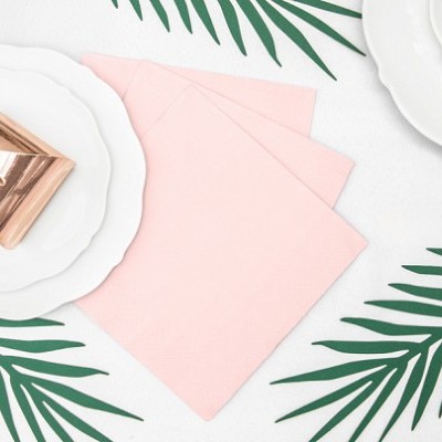 Conjunto de pratos brancos com guardanapos rosa sobre toalha branca com folhas verdes