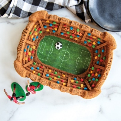 Bolo em forma de estádio de futebol colorido com miniaturas de jogadores e acessórios na mesa