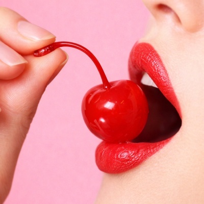 Cereja vermelha com caule perto de lábios vermelhos em fundo rosa