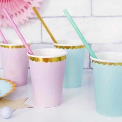 Copos de papel rosa e azul com borda dourada e palhinhas coloridas sobre mesa branca