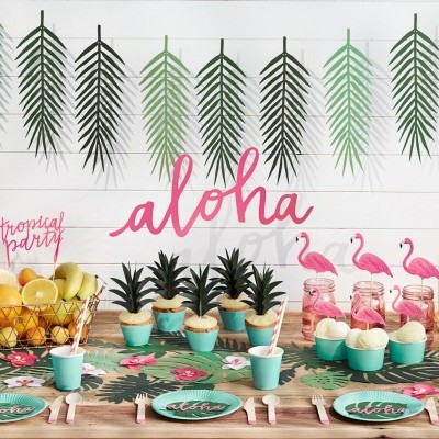 Mesa decorada para festa tropical com abacaxis, flamingos, cupcakes e jarra de bebida.