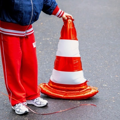 Criança segura cone de trânsito insuflável laranja e branco