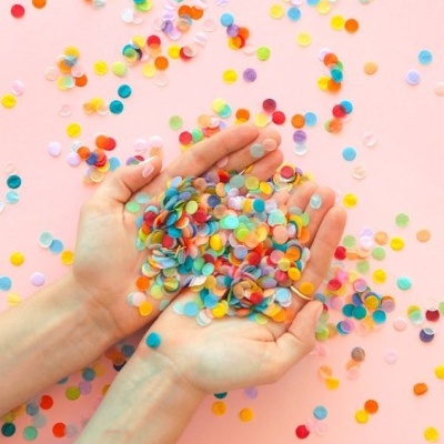 Mãos segurando confetes coloridos redondos sobre fundo rosa claro