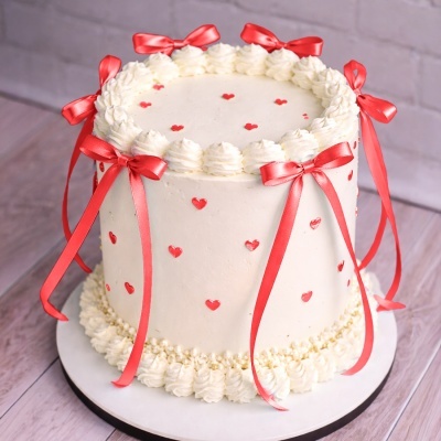 Bolo branco decorado com corações vermelhos e laços de fita vermelha.