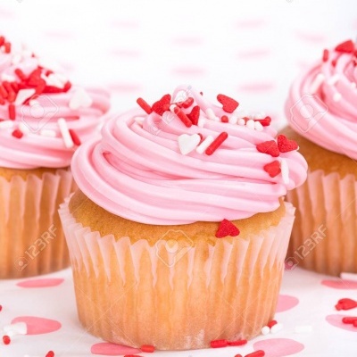 Cupcake com cobertura rosa e granulados vermelhos e brancos sobre superfície com pontos cor-de-rosa