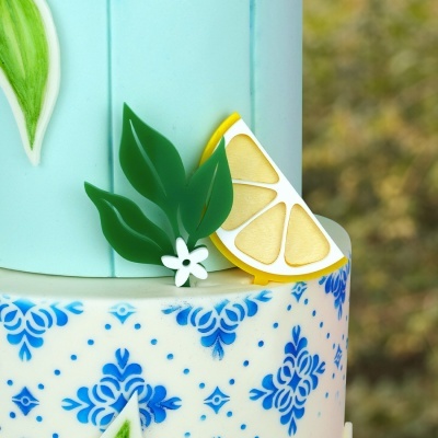Bolo decorativo com padrão azul e decoração de folhas, flor e fatia de limão