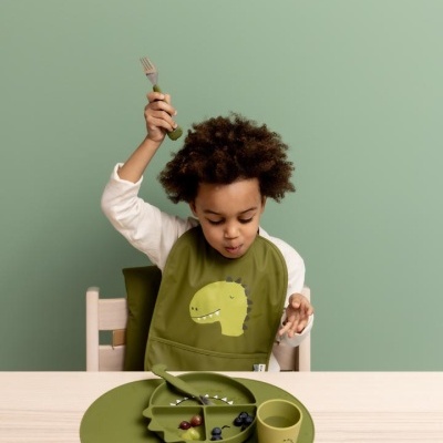 Criança com babete verde e conjunto de refeição infantil dinossauro verde na mesa