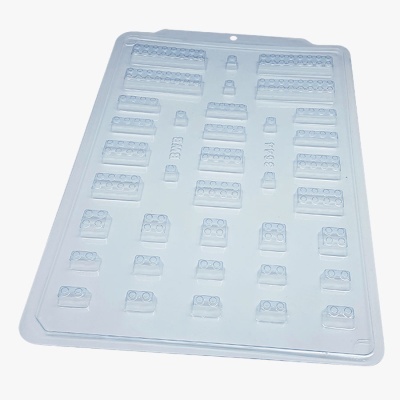 Moldes plásticos transparentes para chocolates em forma de peças tipo LEGO sobre tabuleiro