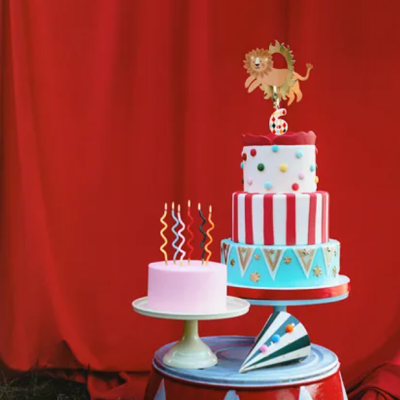 Dois bolos decorados e coloridos sobre tambor vermelho, frente a cortina vermelha