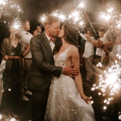 Casal de noivos a beijar-se rodeados por convidados segurando velas de fogo de artifício