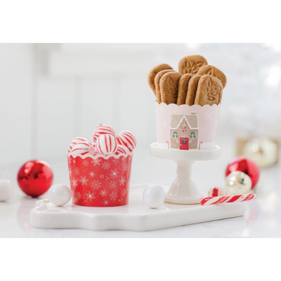 Dois recipientes em porcelana com bolinhas decorativas e biscoitos de gengibre numa superfície branca com bolas de natal ao fundo