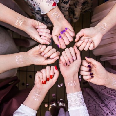 Oito mãos femininas com tatuagens temporárias brancas e unhas pintadas, dispostas em círculo