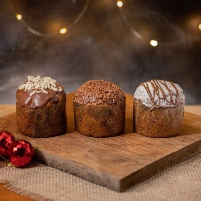 Três mini panetones com diferentes coberturas num tabuleiro de madeira