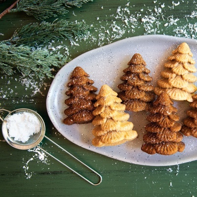 Biscoitos em forma de árvore de Natal com açúcar em pó sobre prato branco e mesa verde decorada
