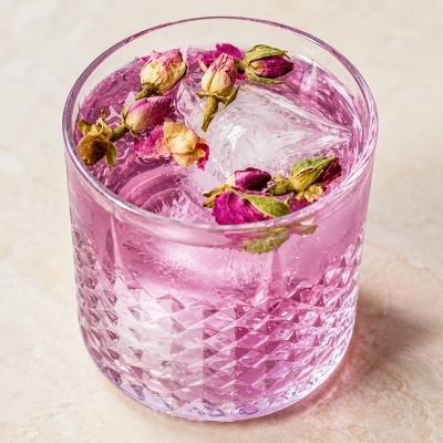Copo de vidro com bebida cor de rosa, gelo e flores secas