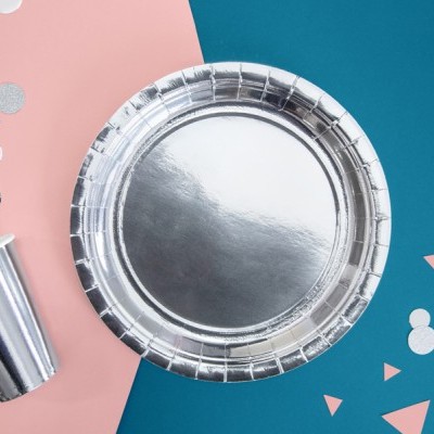 Copo e prato descartáveis prateados brilhantes sobre fundo rosa e azul com confetis