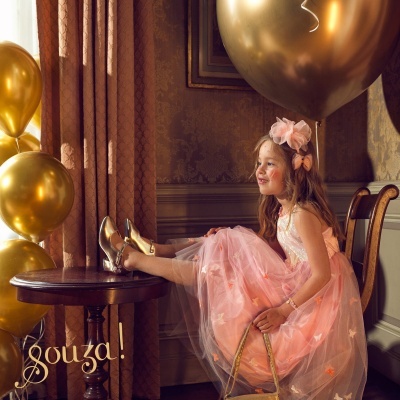 Criança com vestido de festa rosa e sapatos dourados junto a balões dourados