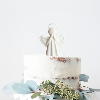 Bolo com cobertura branca e decoração de anjo e folhagem verde.