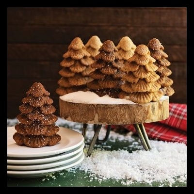 Bolachas em forma de árvore de Natal em cima de base de madeira e prato branco com decoração de neve artificial