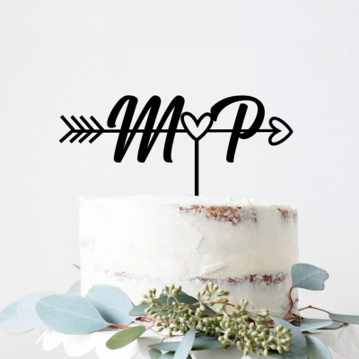 Bolo branco com topo de bolo com letras M e P em preto e decoração de folhas verdes.