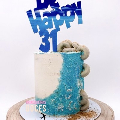 Bolo cilíndrico branco e azul com bastões de decoração e cogumelos sobre base de madeira