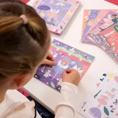 Criança a usar autocolantes coloridos de fadas sobre fundo roxo e rosa numa mesa branca