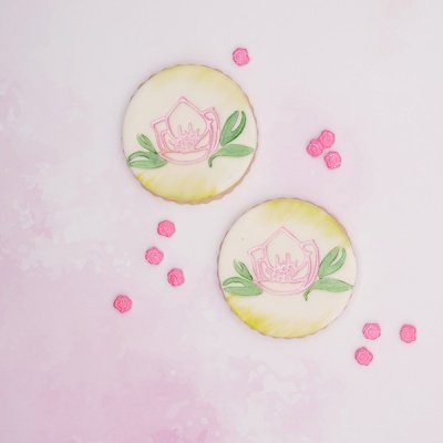 Dois biscoitos decorados com desenho floral rosa e pequenas flores cor-de-rosa num fundo rosa.