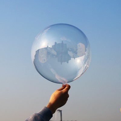 Mão a segurar um balão transparente num céu azul claro