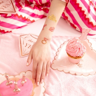 Braço com tatuagens temporárias temáticas de casamento, cupcakes cor-de-rosa e decoração em tecido rosa.