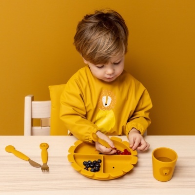Conjunto de alimentação infantil amarelo com prato em forma de leão, copo e talheres em mesa de madeira clara