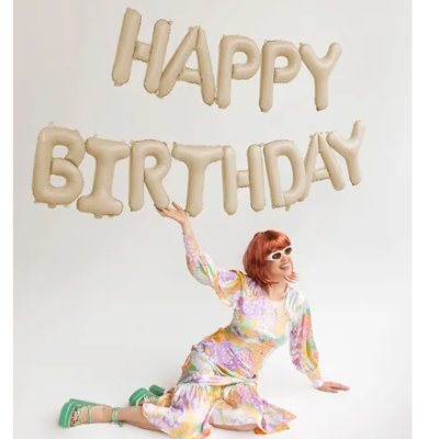 Balões dourados com letras HAPPY BIRTHDAY sobre mulher com vestido colorido em fundo branco