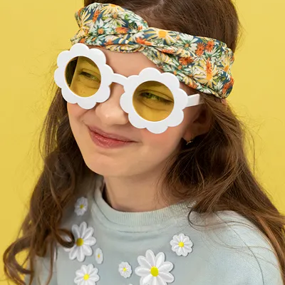 Menina com óculos de sol florais, faixa de cabelo estampada e camisola com aplicações de flores.